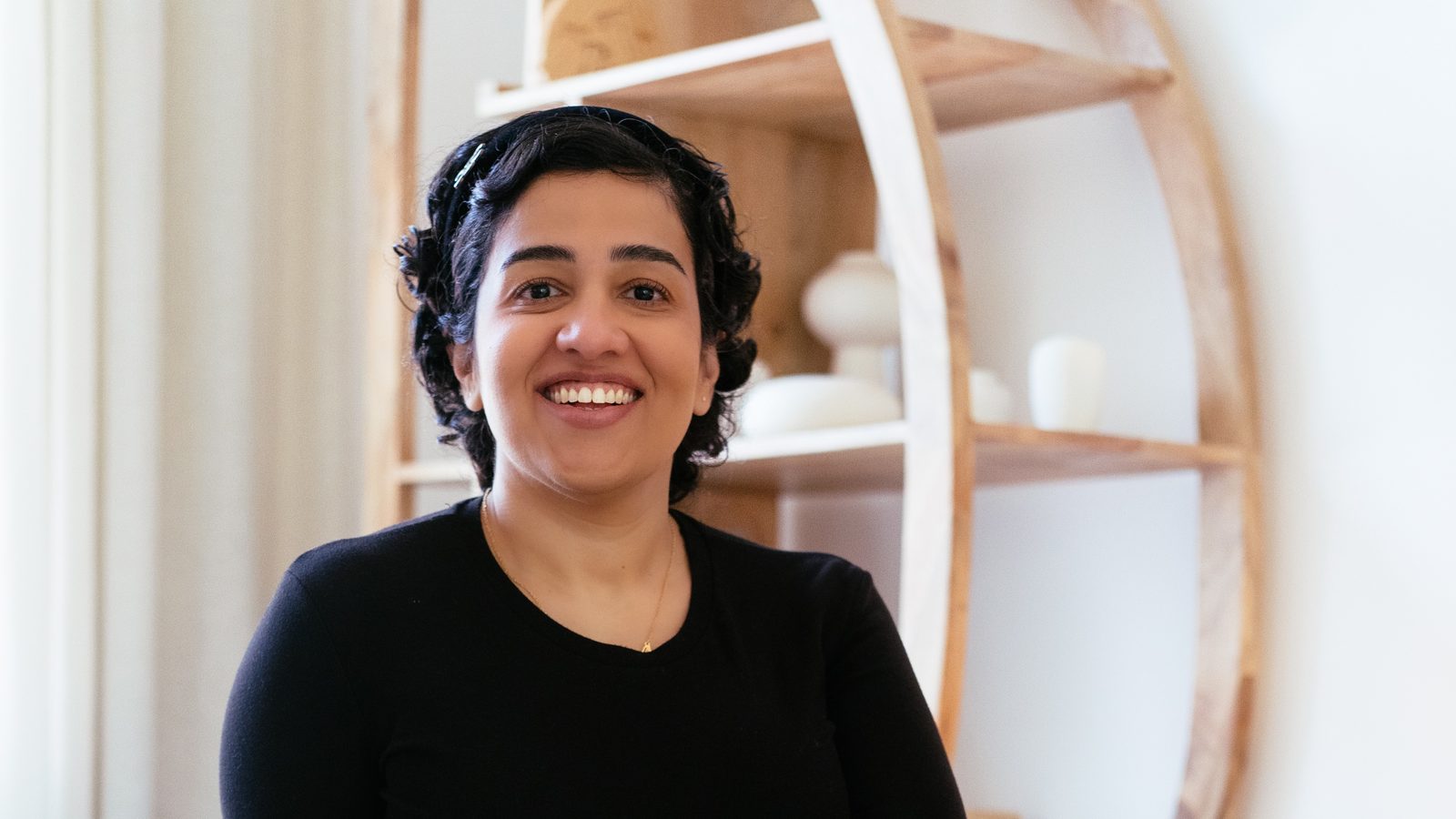 Rucha Daryani, author of The Light Never Left and founder of The Second Act, smiling in front of a curved wooden shelf