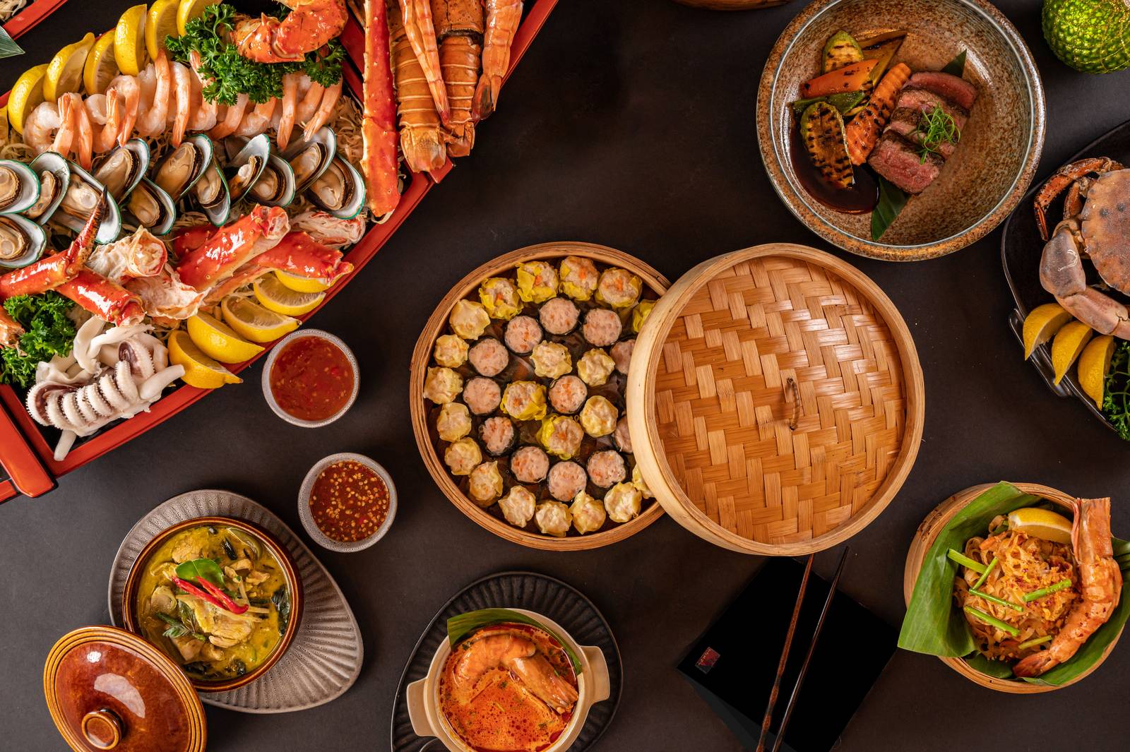 An overhead view of a table laid with seafood, bamboo steamer baskets of dumplings, sushi rolls and small bowls of Asian dishes