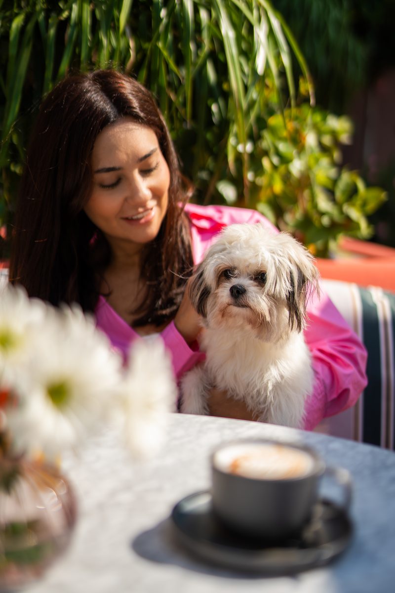 A woman smiling at a small dog seated beside her at a cafe table