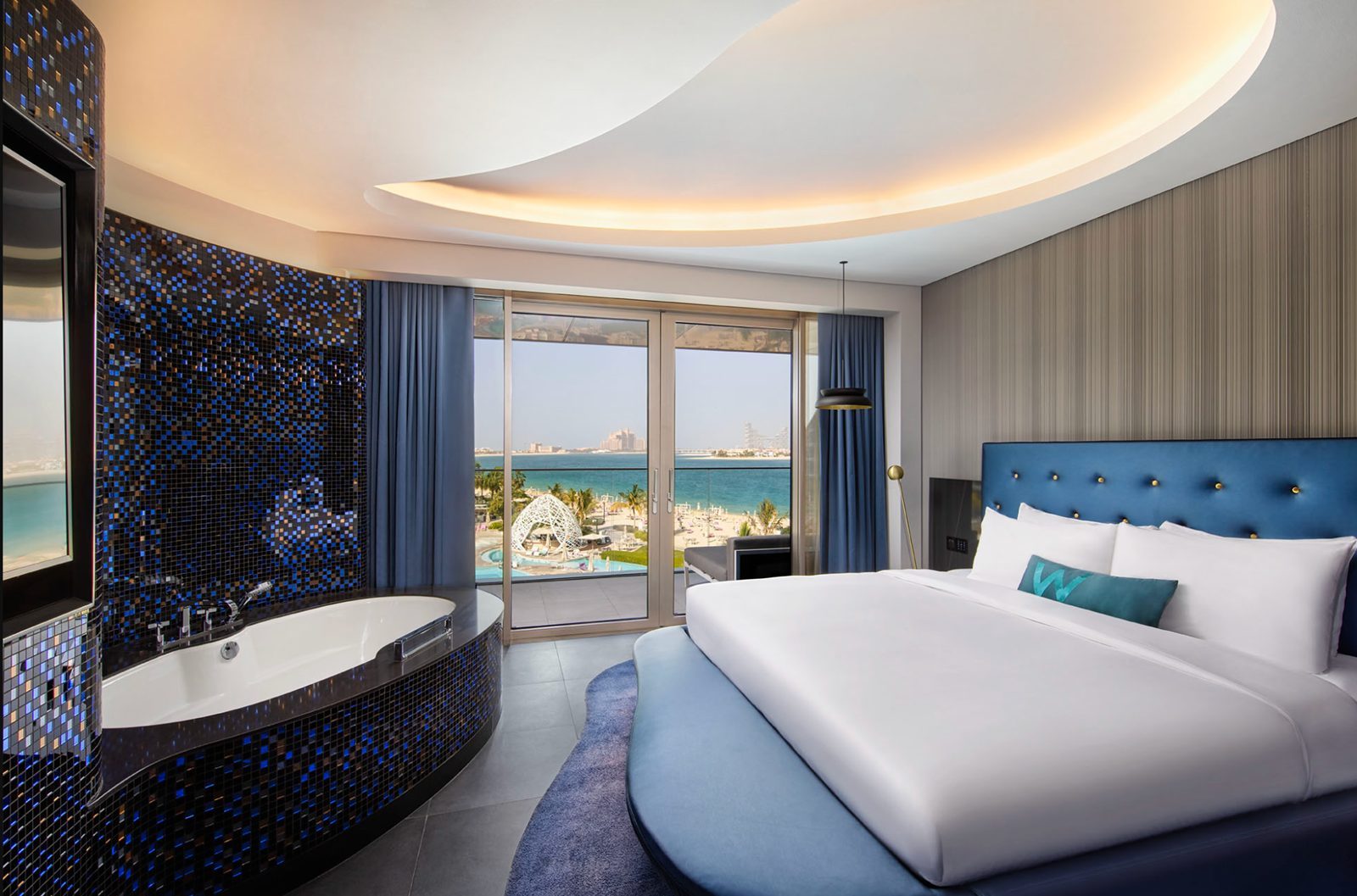 A suite bedroom at W Dubai The Palm with a bathtub by the window and a balcony looking out over the pool and the sea