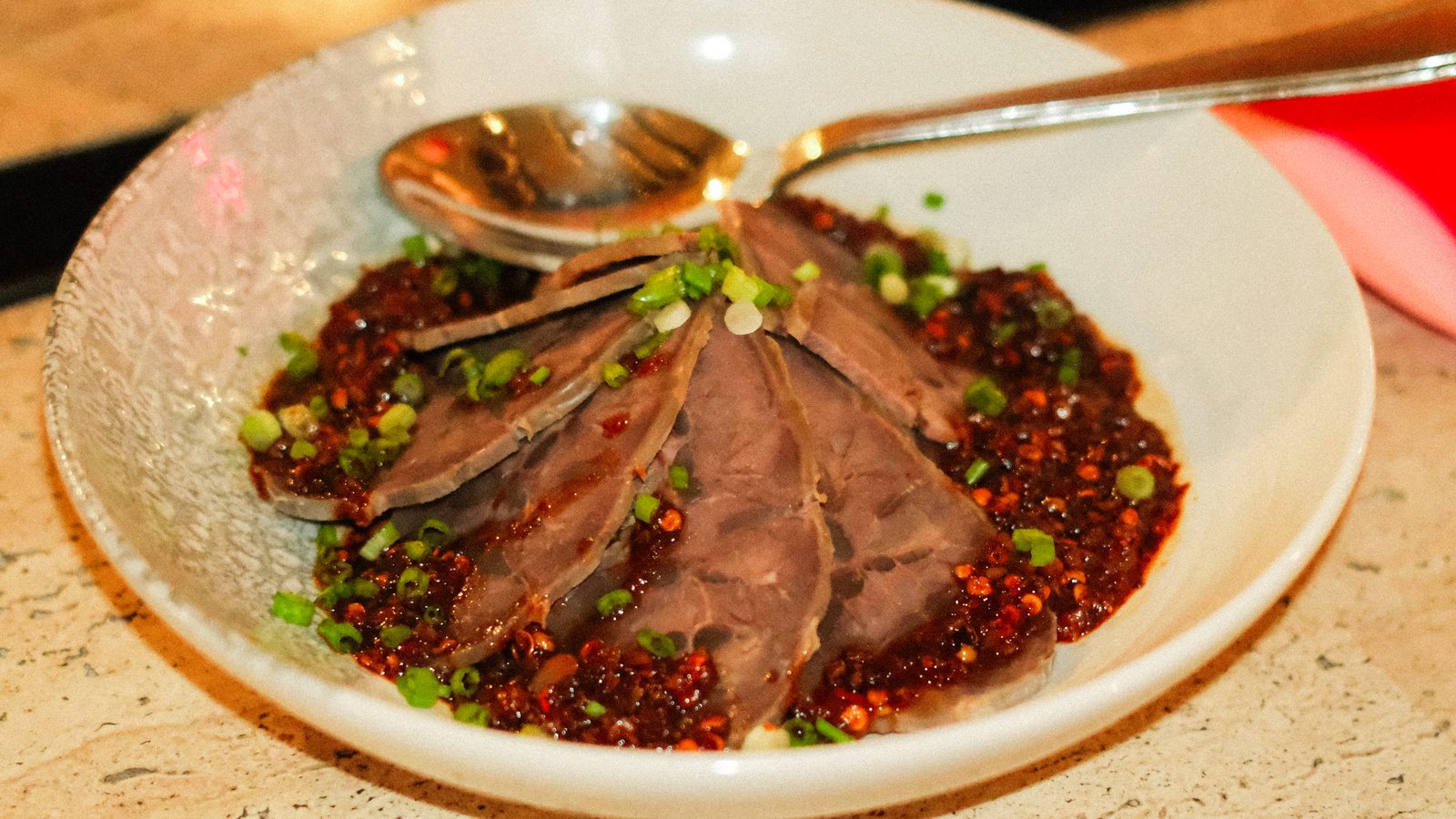 A white bowl of sliced meat in red chilli oil topped with spring onion, from an earlier XVA x Five Spice Supper Club